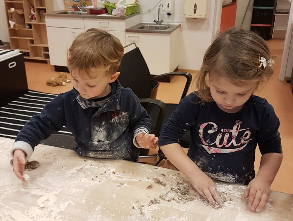 Twee peuters kneden deeg op een tafel vol bloem