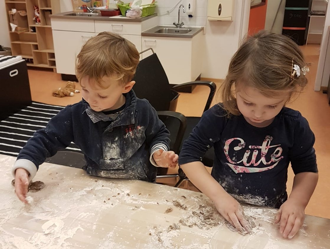 Een jongen en een meisje kneden samen koekjesdeeg aan een tafel vol bloem
