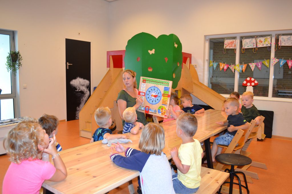 Een pedagogisch medewerker laat de peuters de dagklok zien
