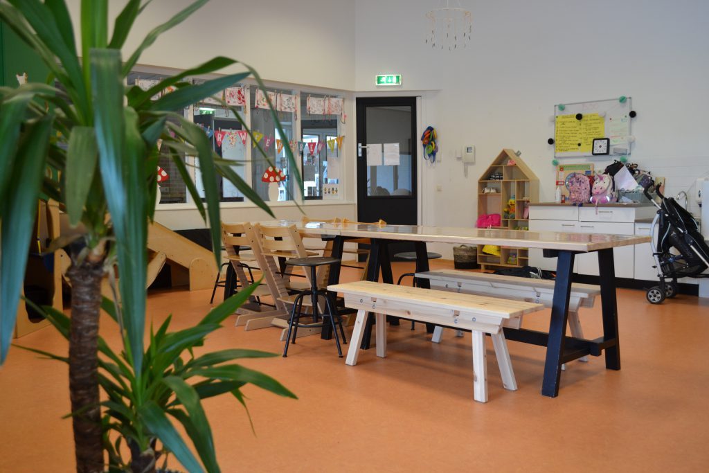 De peuterruimte met een lange houten tafel en vlaggetjes voor het raam