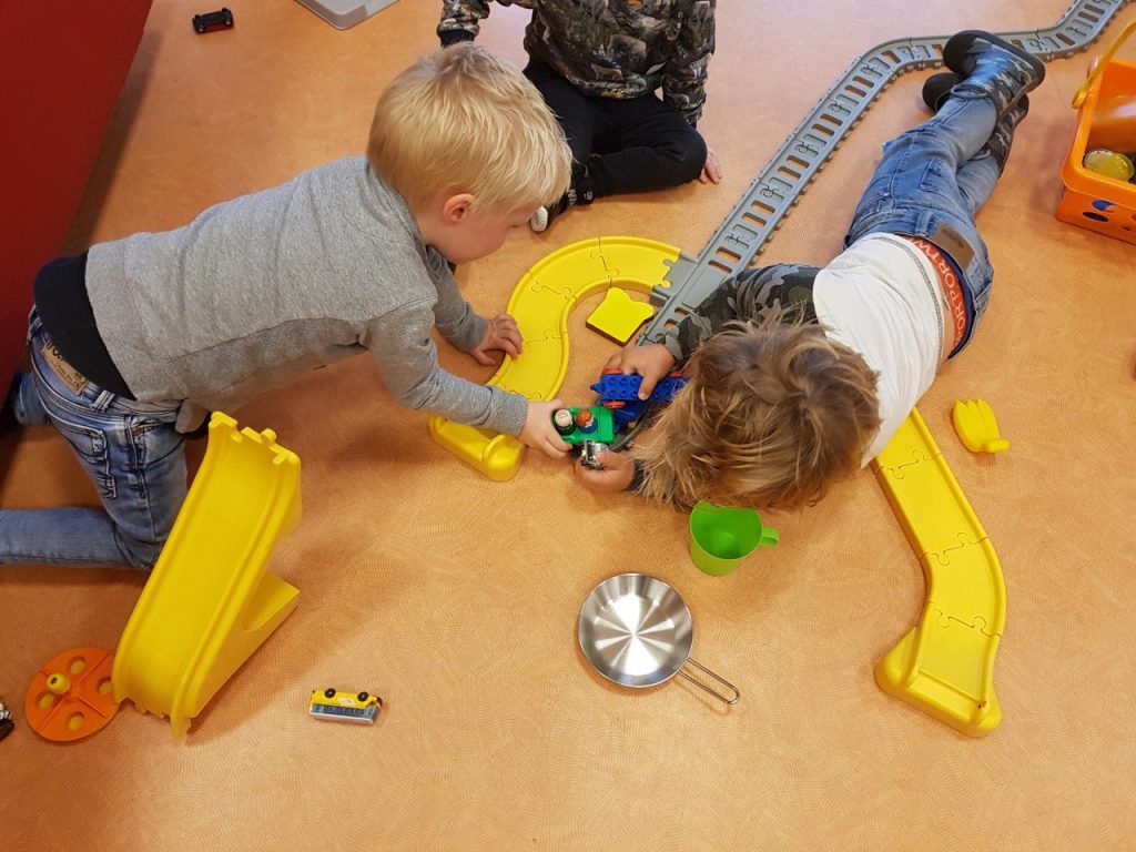 Twee jongens bouwen samen een treinbaan op de vloer