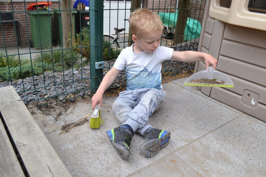 Jongetje veegt de tuin met stoffer en blik
